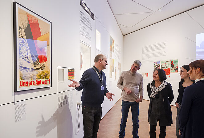 Ein Mann gibt eine Führung und steht vor einer Ausstellungswand.